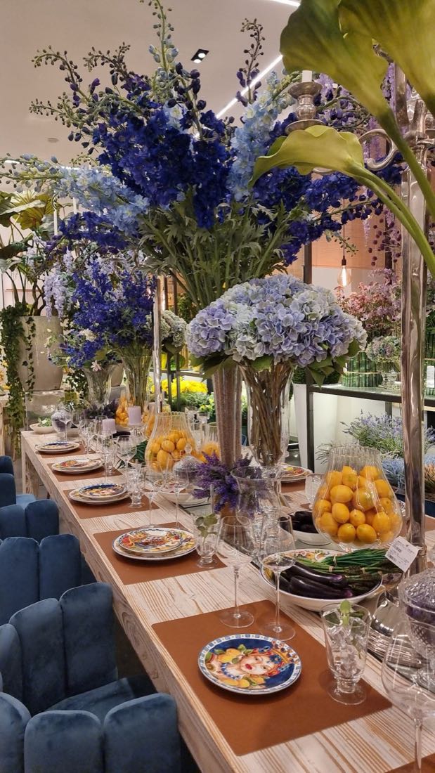 Masă festivă lungă, cu aranjamente de hortensii și delphinium albastru, farfurii pictate și lămâi